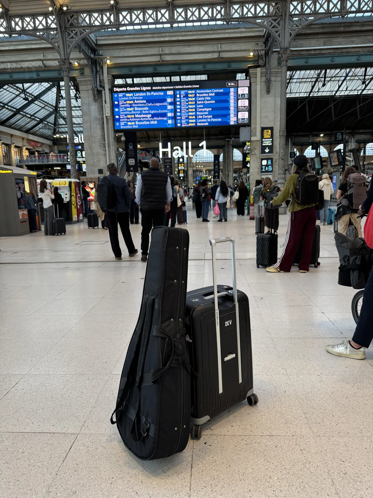 Guitar case and suitcase beneath the departure board in a railway station