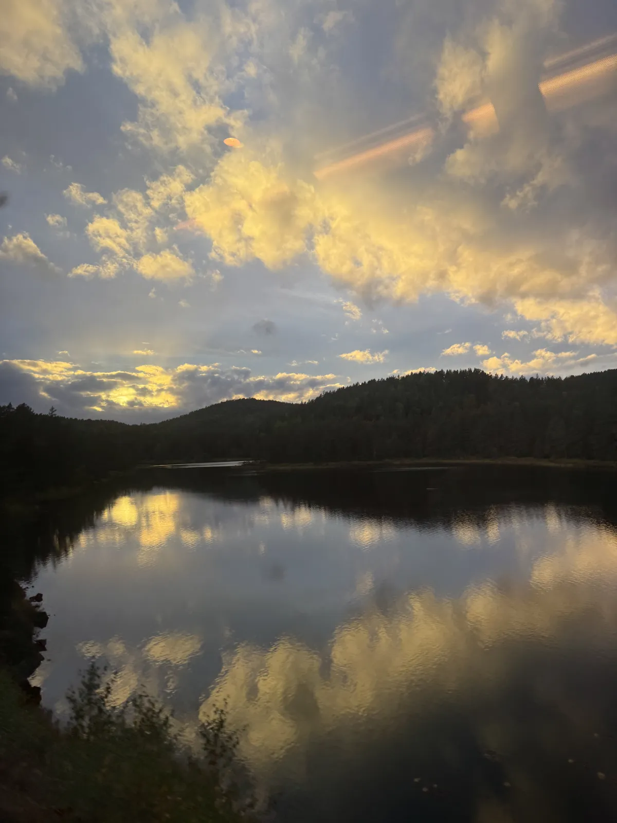 Golden clouds and Norwegian hills reflected in a lake, seen from the train